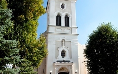 Fragment kościoła z gł&oacute;wnym wejściem i wieżą, obok drzewa