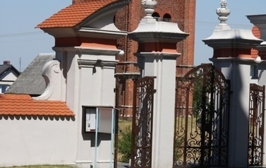 Brama, za kt&oacute;ra znajduje się dzwonnica z czerwonej cegły
