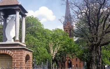 Na pierwszym planie kapliczka z figurą Maryi, w oddali budynek kościoła