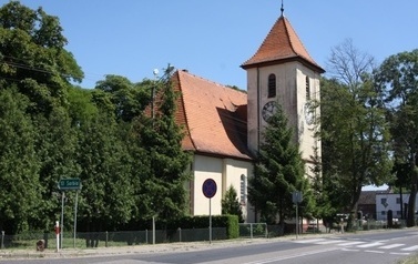 Budynek kościoła położony przy drodze, z lewej strony liściaste drzewa