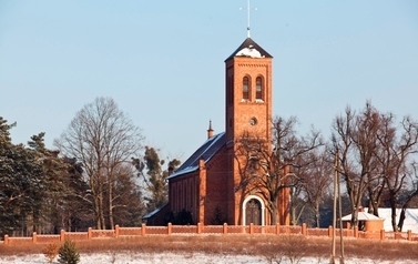 W oddali budynek kościoła z czerwonej cegły, wok&oacute;ł drzewa w zimowej odsłonie