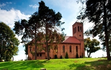 Na pierwszym planie drzewa, za drzewami budynek kościoła z czerwonej cegły