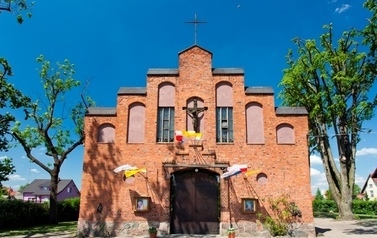 Budynek kościoła z czerwonej cegły, za kościołem dwa drzewa