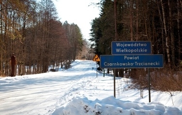Droga publiczna pokryta śniegiem z tablicą z napisem wojew&oacute;dztwo wielkopolskie powiat czarnkowsko-trzcianecki