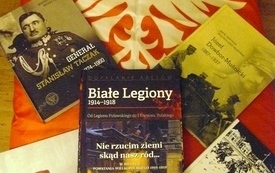 Na pierwszym planie historyczne pozycje książkowe; w tle czerwona flaga z białym orłem