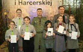 Pomieszczenie; na pierwszym planie sześć dziewczyn ubranych w mundury harcerskie, w rękach trzymają dyplomy. Za nimi dw&oacute;ch mężczyzn, jeden z nich też w harcerskim mundurze.
