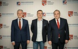 Pomieszczenie; na pierwszym planie trzech mężczyzn; wszyscy odświętnie ubrani; w tle herb powiatu czarnkowsko-trzcianeckiego oraz logo Forum Gospodarczego.