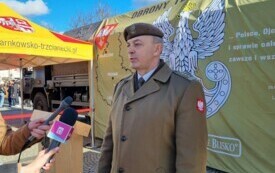 Plener; na pierwszym planie pułkownik Dariusz Wyrzykowski udzielający wywiadu. Za jego plecami baner obrony terytorialnej.