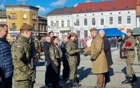Plener; na pierwszym planie pułkownik gratulujący młodej żołnierce wyr&oacute;żnienia za osiągnięcia podczas szkolenia.