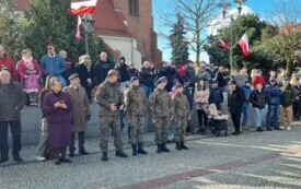 Plener; na pierwszym planie zebrani goście - rodziny i znajomi żołnierzy składających przysięgę. W tle powiewają biało-czerwone flagi.