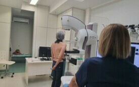 Pomieszczenie; na pierwszym planie kobieta stojąca przy mammografie.