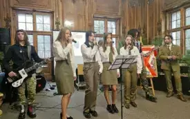 Pomieszczenie, na pierwszym planie kobieta w zielonej marynarce, przemawia do mikrofonu. Tuż obok niej mężczyzna w mundurze leśnika. Obok nich choinka przybrana światełkami. Na ścianie obraz z widokiem na zamek Hochberg&oacute;w.