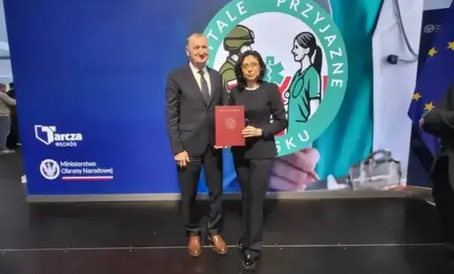 Elegancko ubrani mężczyzna i kobieta stoją na tle wyświetlonego slajdu, kobieta trzyma czerwoną teczkę.