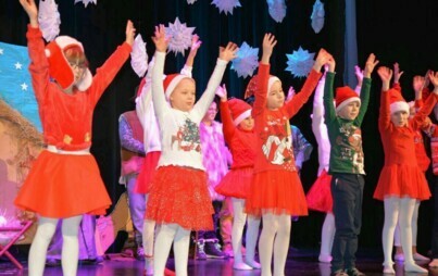 Pomieszczenie; na scenie dzieci ubrane głównie na czerwono, wszystkie trzymają ręce uniesione do góry.